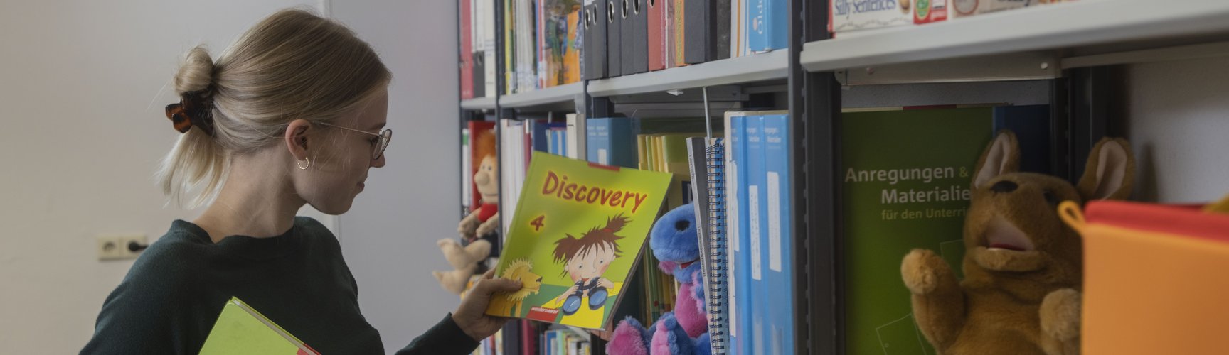 Eine Studentin nimmt ein Arbeitsheft aus einem Bücherregal