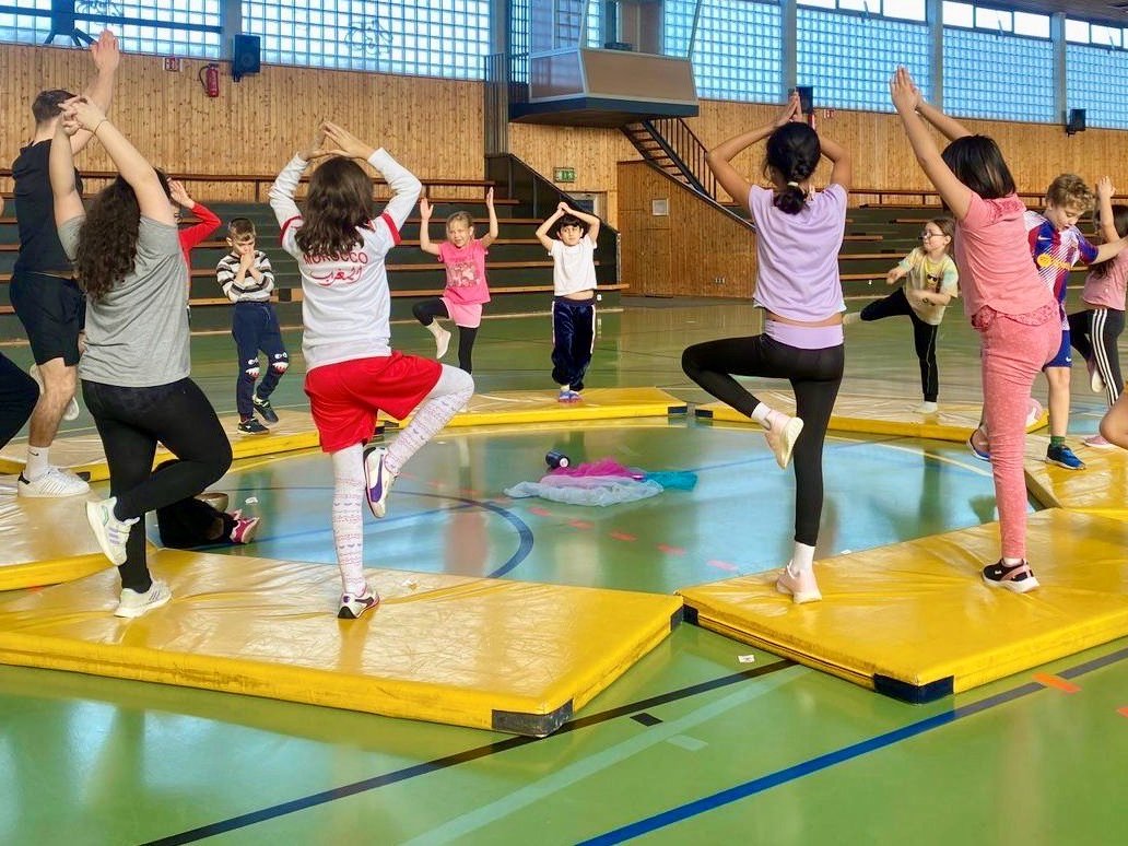 In einer Sporthalle machen Kinder auf Matten Streck- und Balanceübungen