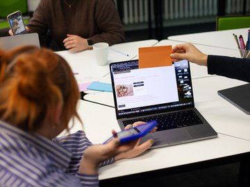 Schülerinnen vor einem Laptop und analogen Bildchen in der Hand beschäftigen sich mit KI im Kustunterrichtsich mit 