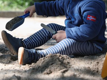 Ein KiTa-Kind sitzt im Sand und hantiert mit einer Schaufel