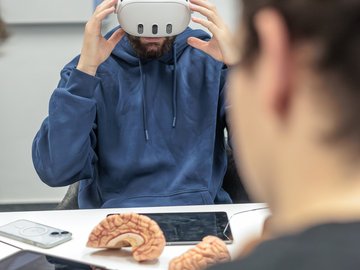 Männliche Person mit VR Brille sitzt an einem Tisch