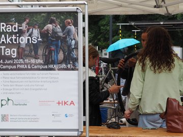 Drei junge Frauen reparieren ein Fahrrad, im Vordergrund ein Plakat des Rad-Aktions-Tags