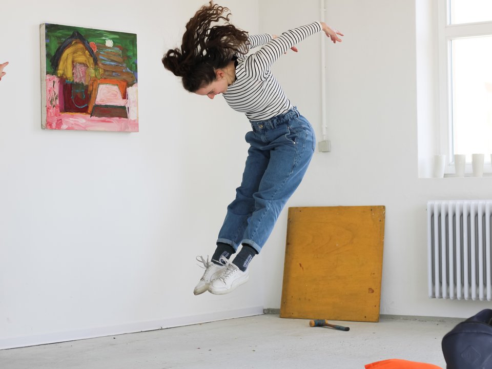 Eine Studierende des MA Kult springt vor einem Bild in die Höhe