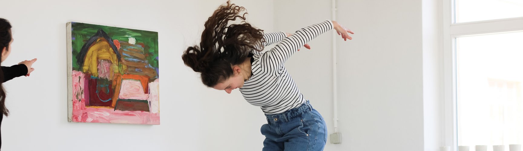Eine Studierende des MA Kult springt vor einem Bild in die Höhe