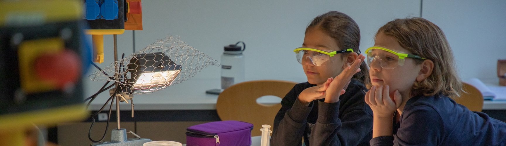 Zwei Grundschulkinder mit Schutzbrille verfolgen ein physikalisches Experiment