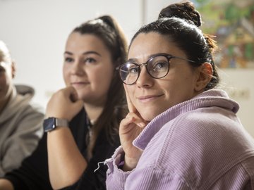 Eine Studierende schaut freundlich in die Kamera, im Hintergrund sind Kommilitoninnen erkennbar