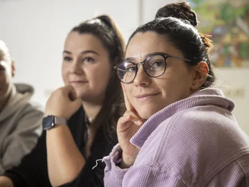 Eine Studierende schaut freundlich in die Kamera, im Hintergrund sind Kommilitoninnen erkennbar