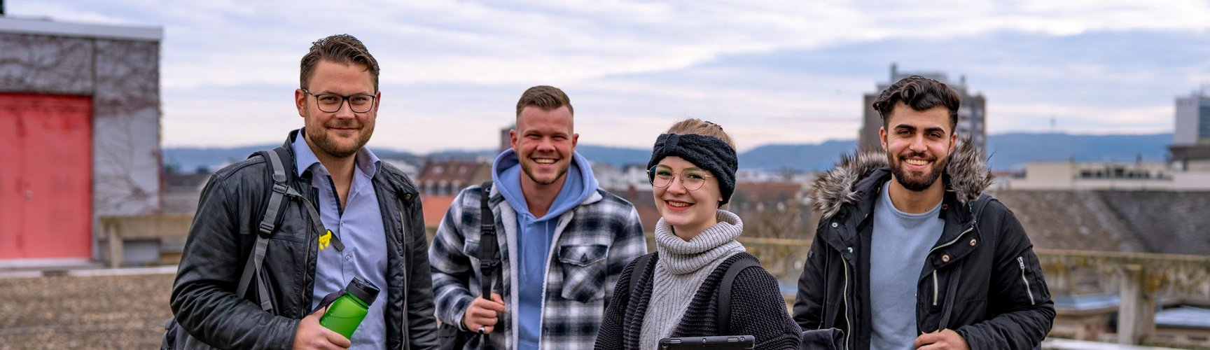 Vier Studierende stehen auf dem Dach der Hochschule und lachen in die Kamera