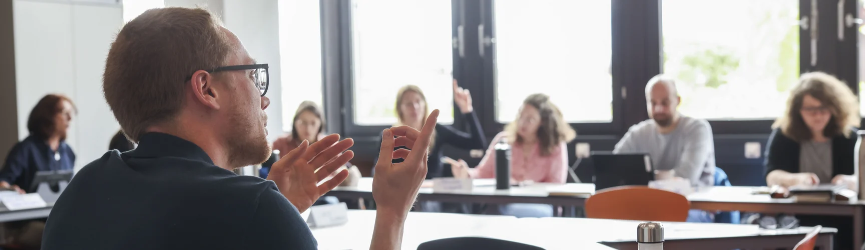 Szene aus einer Weiterbildungsveranstaltung: Personen sitzen in einer Runde und diskutieren, ein Mann im Vordergrund spricht gerade