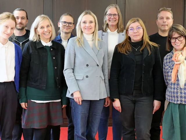 Gruppenfoto von neun Personen verschiedenen Alters und Geschlechts.