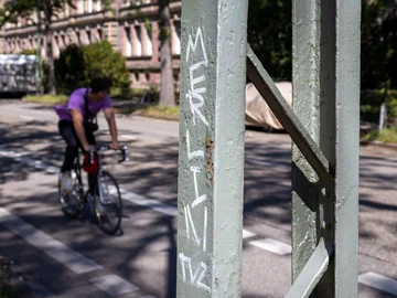 Pfosten mit Graffiti, im Hintergrund ein Radfahrer auf einem Rennrad