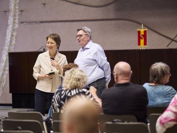 Bürgermeisterin Lisbach und Rektor Rippe stehnd im informellen Gespräch vor Publikum, das von hinten sitzend zusehen ist.ten zu