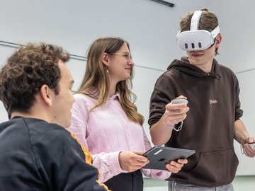 Drei Personen interagieren, eine davon trägt eine VR Brille