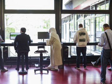 Mehrere Personen arbeiten an der Hochschule an PCs an Steharbeitsplätzen.