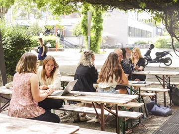 Eine Gruppe Studierender sitzt an Biertischen vor der caphete der Hochschule