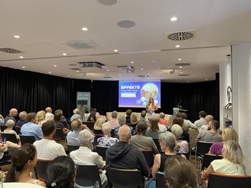 Publikum von hinten beim EFFEKTE-Abend am 11. August 2026 mit Moderatorin.