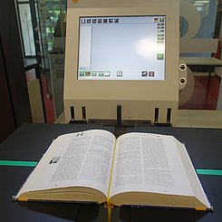 Man sieht ein aufgeschlagenes Buch auf einem Buchscanner liegen.