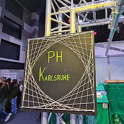 In der Halle der Science Days hängt eine quadratische Schiefertafel, in der Mitte steht in hellgrün "PH Karlsruhe", um die Schrift ist mit Schnur ein Netz gespannt.