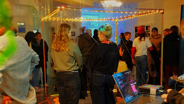2026_02_11_Kunst im Jubez Situation auf der Kunstausstellung mit ein paar Personen, die eine Installation bettrachten, und weiteren im Hintergrund.