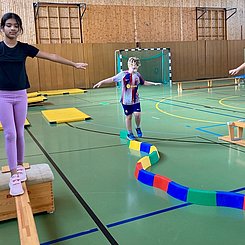 In einer Sporthalle balancieren Kinder auf verschiedenen Geräten