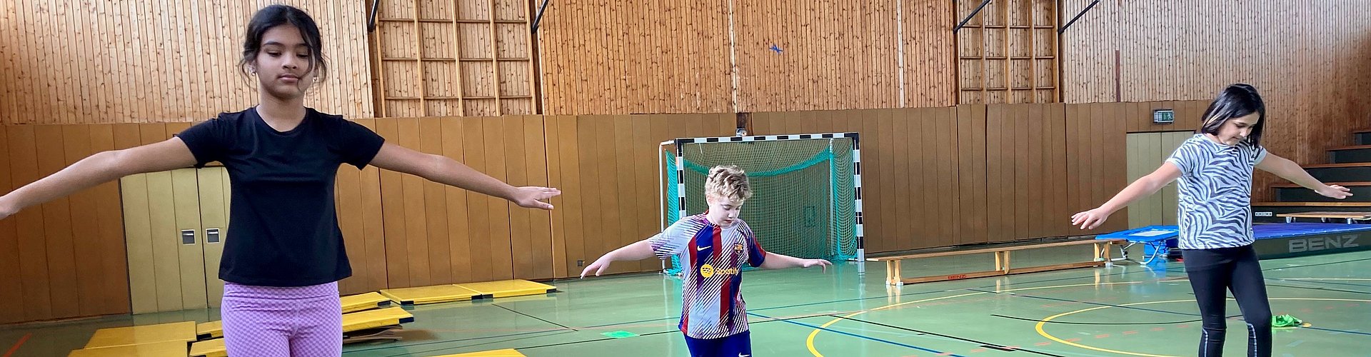 Kinder machen Balancierübungen in einer Sporthalle